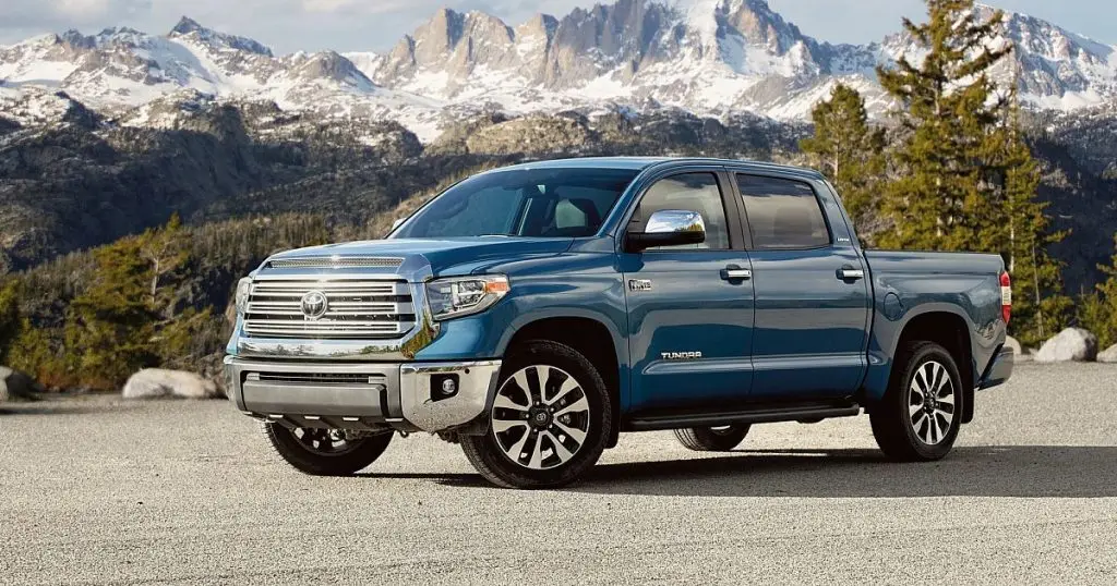 Blue Toyota Tundra pickup truck parked before snow-capped mountains and pine trees