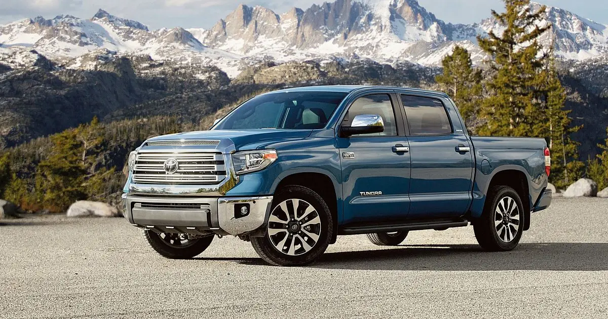 Blue Toyota Tundra pickup truck parked before snow-capped mountains and pine trees