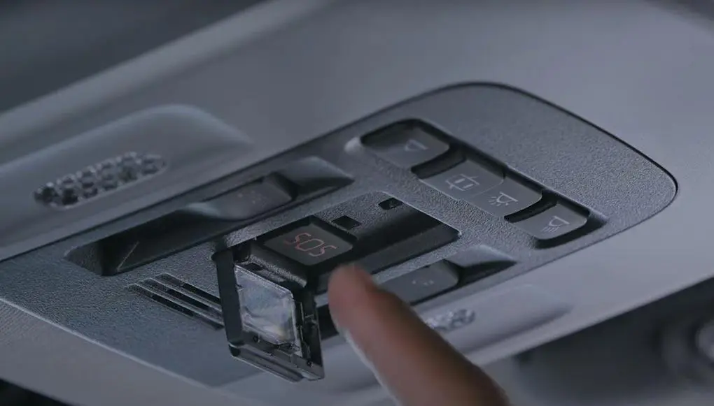 Finger pressing the red SOS emergency button on a vehicle's overhead console