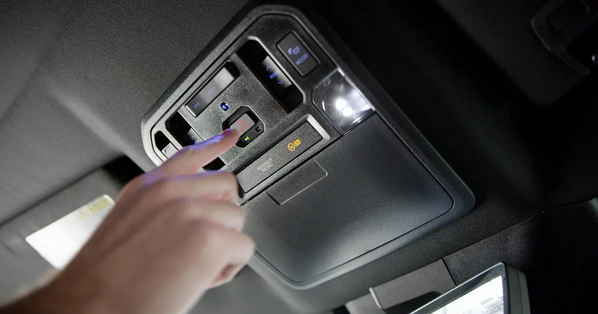 Finger pressing the SOS emergency button on a vehicle's overhead console