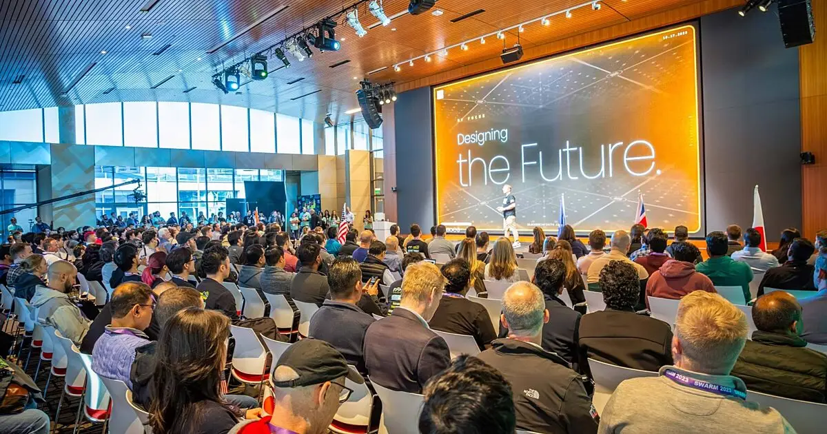 Audience seated facing a large stage screen reading Designing the Future at a conference